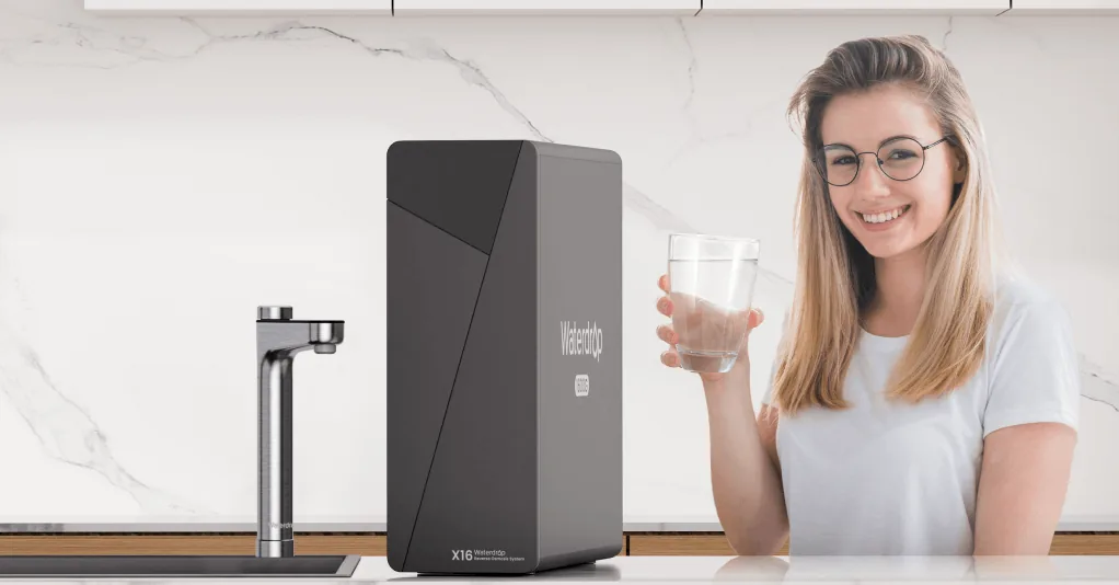 Femme tenant un verre d'eau filtrée à côté de l'osmoseur Waterdrop X16 dans une cuisine
